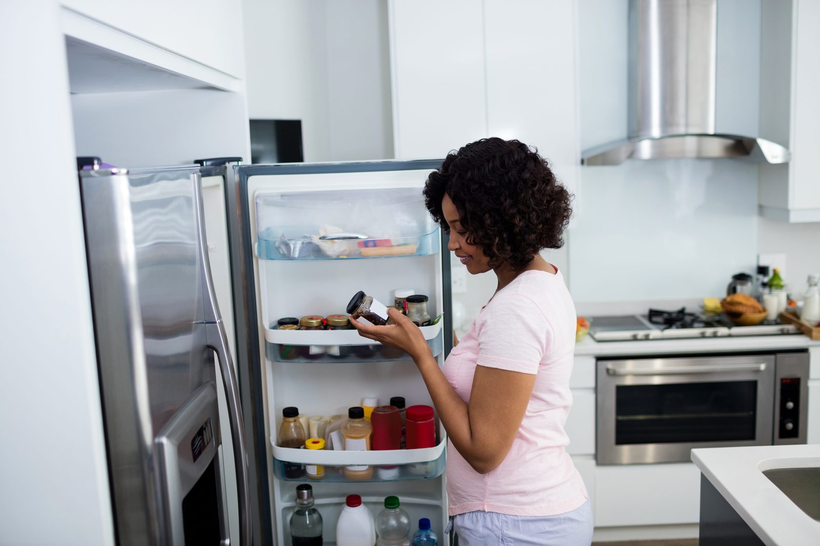 Woman inspecting a jar of food at an open fridge